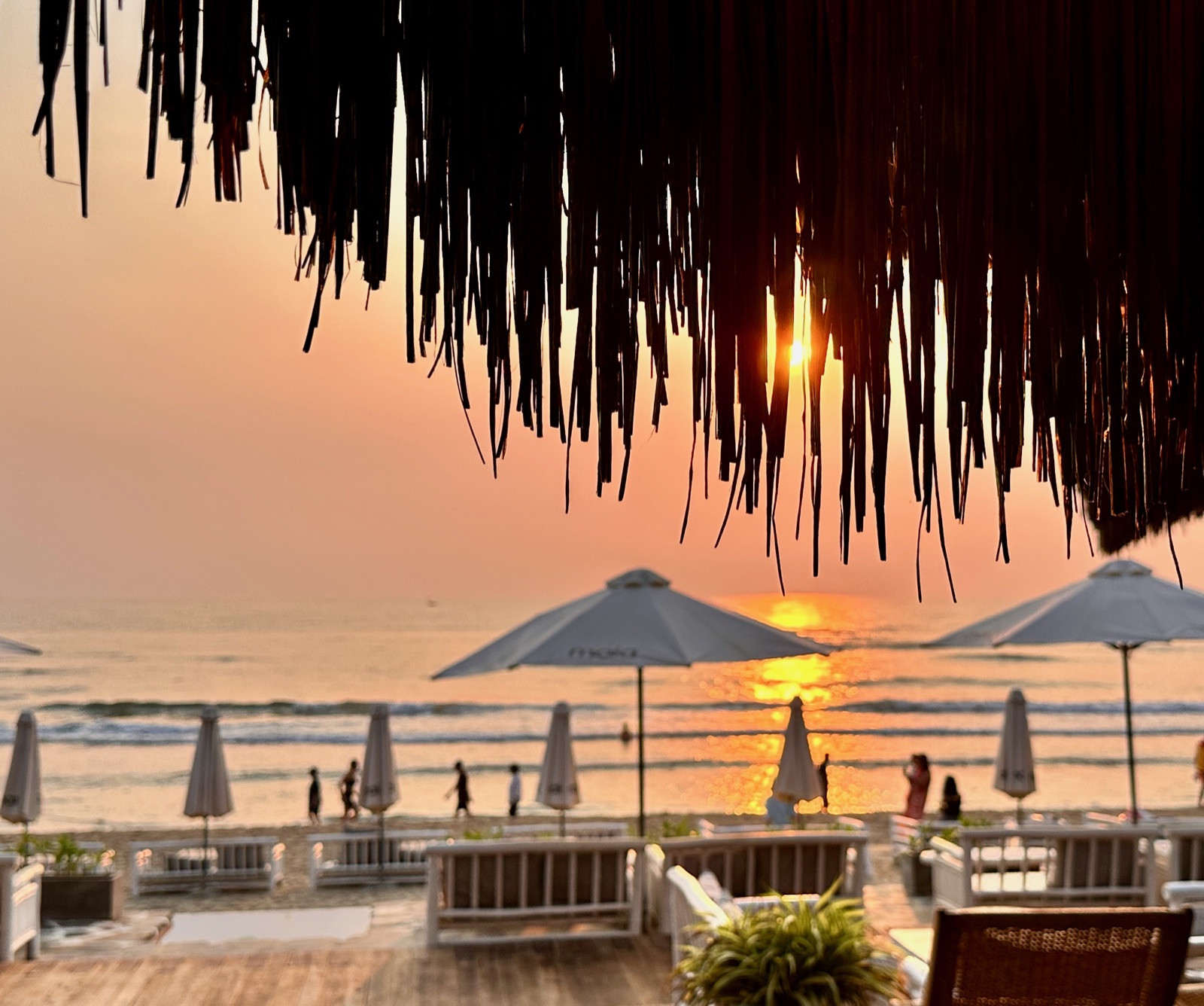Golden sunrise seen through a thatched beach canopy over the Da Nang coast
